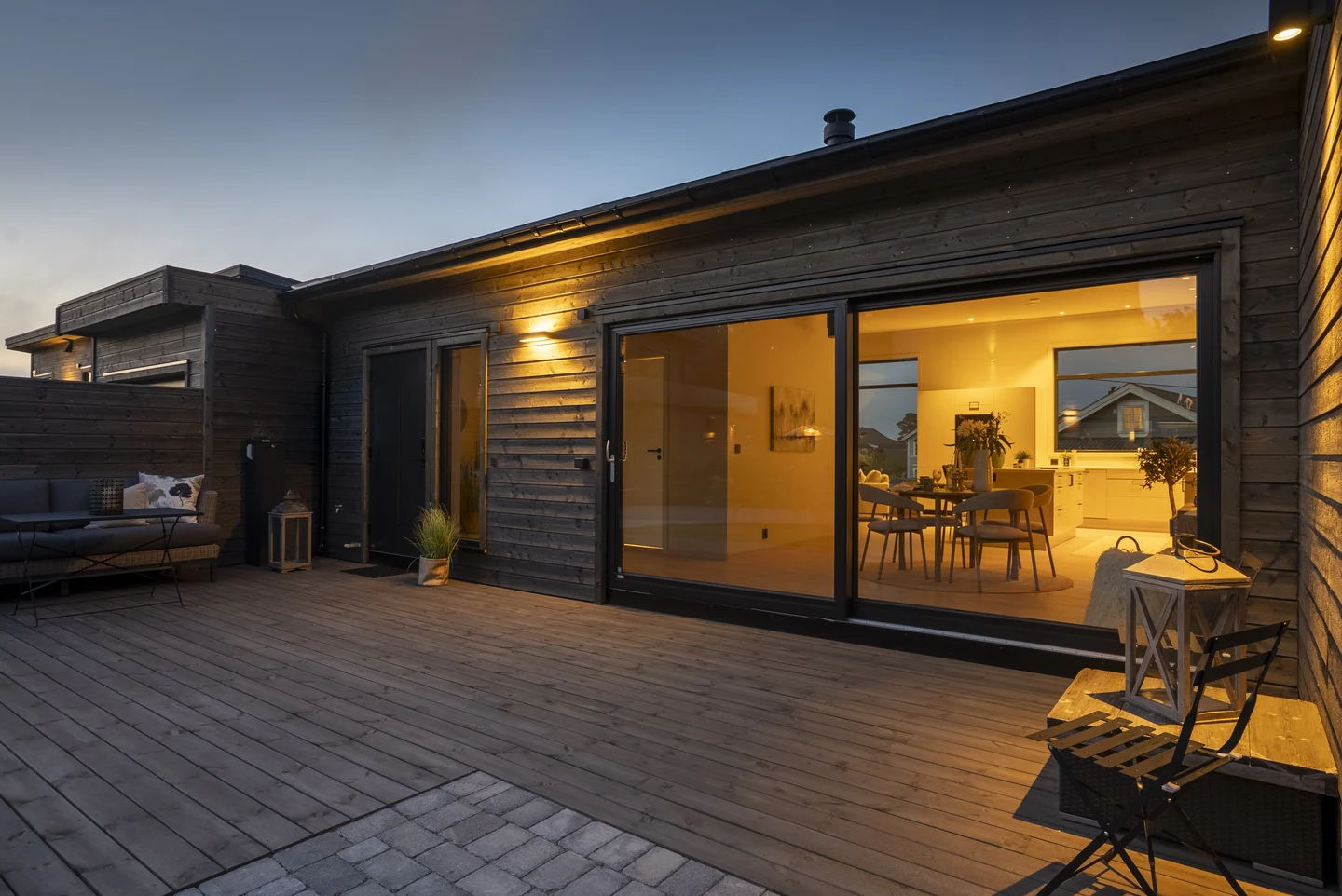 Ringshaughøyden 11 med terrasse og opplyst stue og kjøkken i kveldslys.