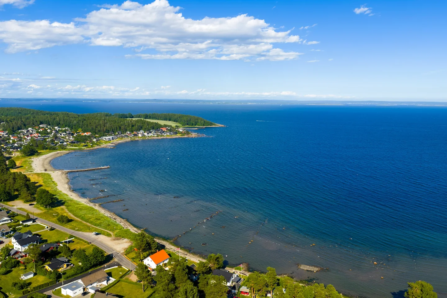 Dronefoto av Skallevoldstranda med sandstrand, molo, grøntområder og sjø